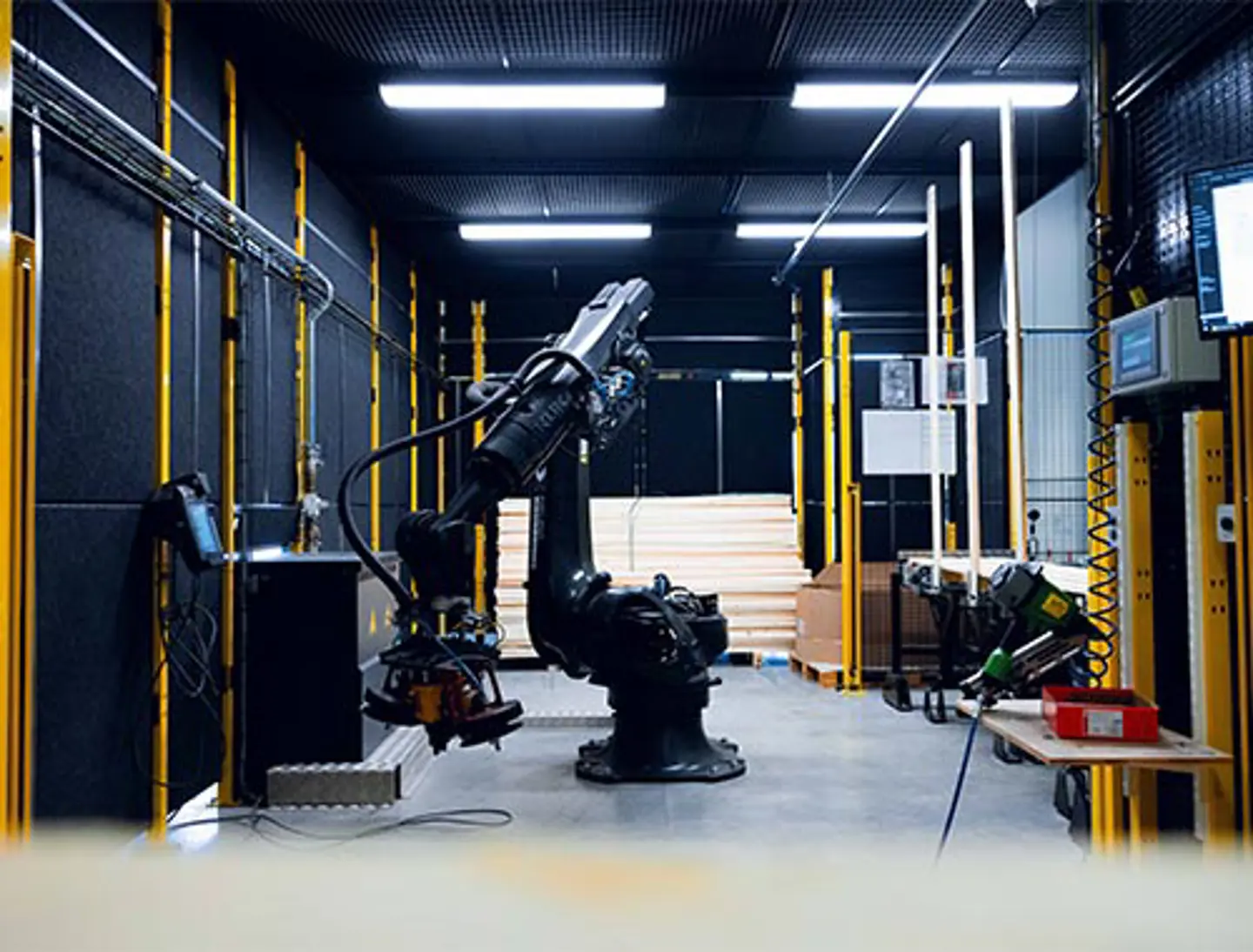A rectangular black sheet metal panel is fastened to a yellow metal posts, forming part of a protective enclosure around an automated robot.