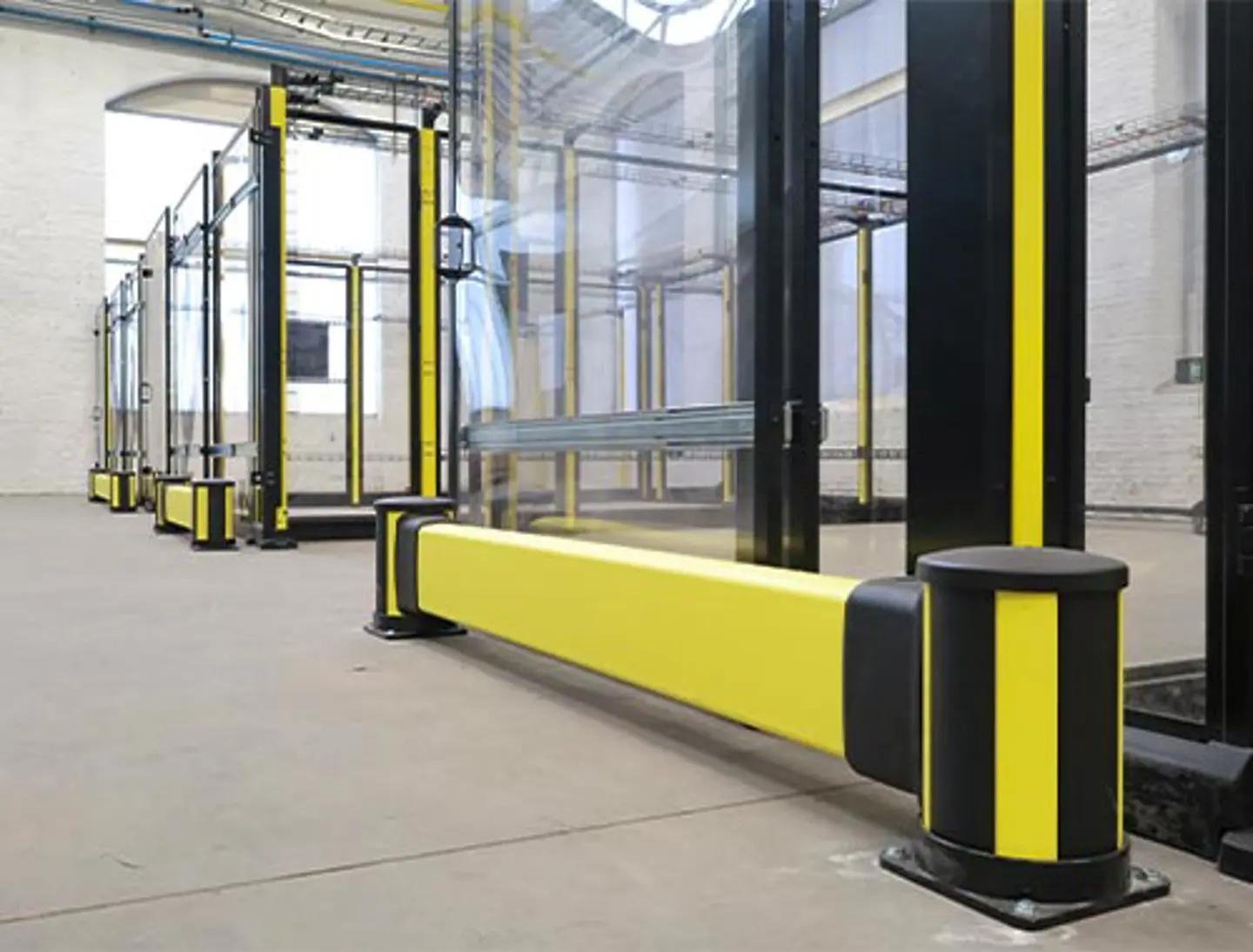 "A metal safety fence with upright posts surrounds industrial equipment in a warehouse setting.